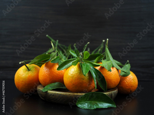 Many fresh tangerines with leaves on a wooden vintage plate, on a dark background. Close up