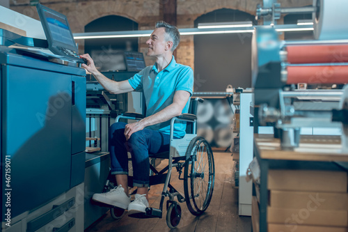 Man in wheelchair touching control panel of office equipment