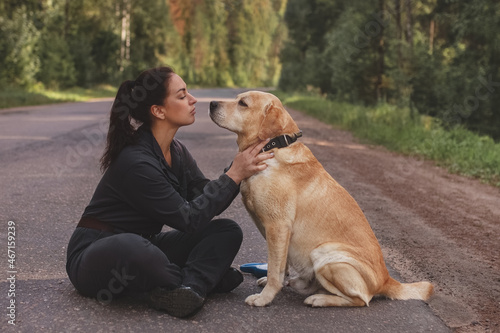 brunette woman sitting on road opposite her Labrador dog