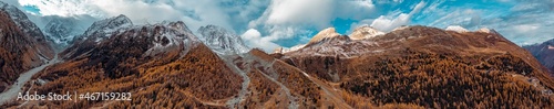 Amazing views over an high alpine valley and snow covered mountains. Orange and yellow coloured autumn and fall trees line the valley sides as the peaks rise above the clouds in this wilderness.
