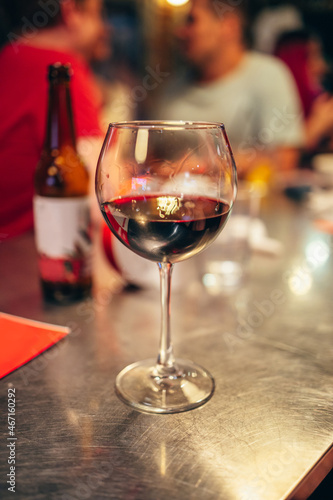 A glass of red wine stands on a metal table in the bar. Blurry people talking in the background. The atmosphere of the bar-restaurant. Alcohol.