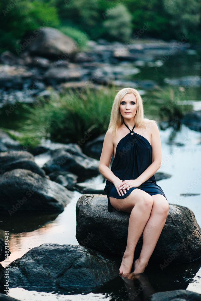 blonde girl in a black dress with blue eyes on the coast of the river