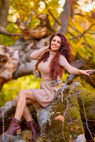 a beautiful woman posing on a log of an old tree in autumn, the colors of autumn