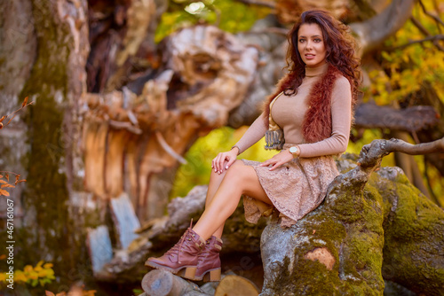 a beautiful woman posing on a log of an old tree in autumn, the colors of autumn