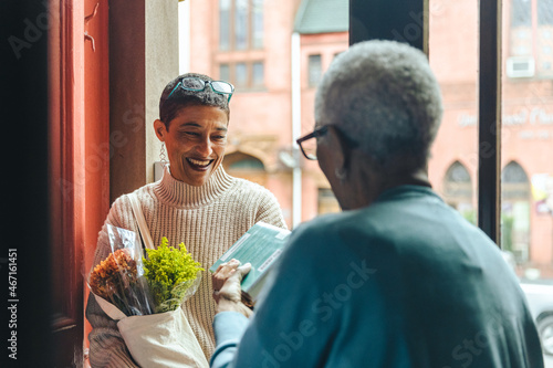 Smiling adult woman visiting an elderly person in her home with flowers and groceries