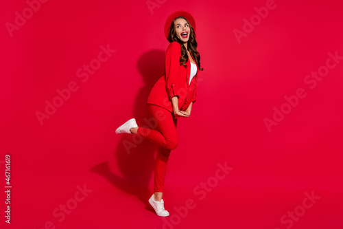 Full length profile photo of cool brunette lady look empty space wear cap suit shoes isolated on red color background