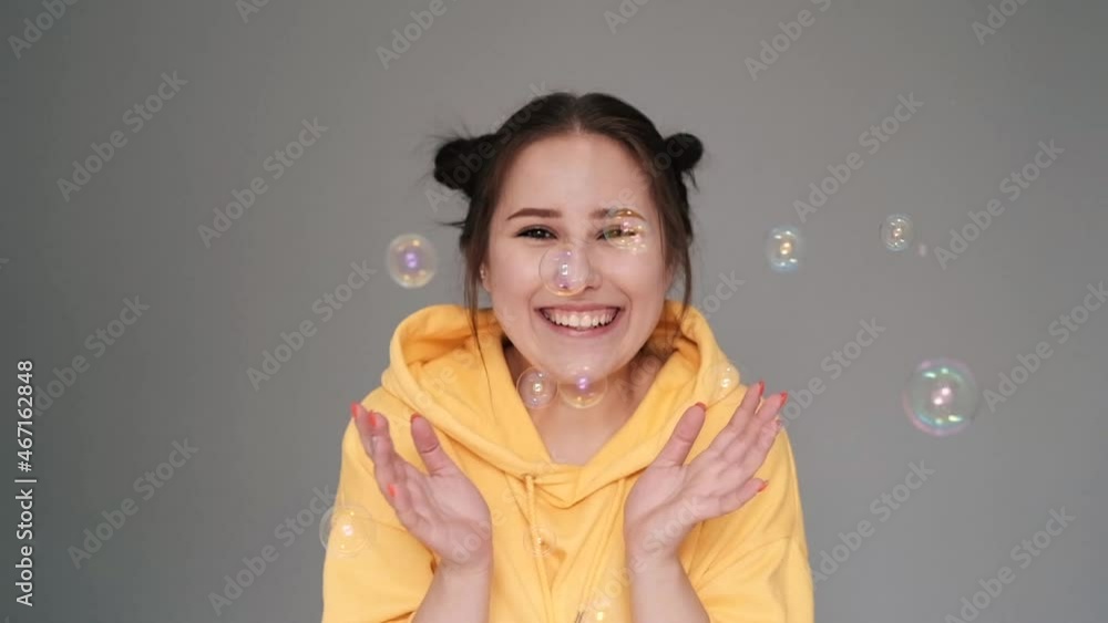 happy brunette woman in yellow hoodie among soap bubbles in bright grey room. happy people. millennial generation. fashionable teenager. trendy colours. slow motion. happy brunette woman in yellow hoodie among soap bubbles in bright grey room. happy people. millennial generation. fashionable teenager. trendy colours. slow motion.