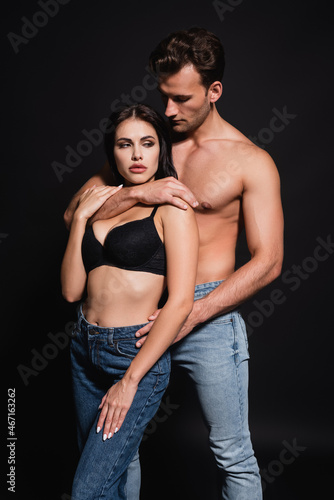 sexy man hugging seductive woman in jeans and bra on black