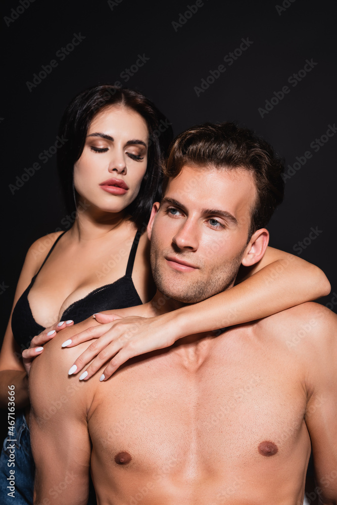 passionate brunette woman in bra embracing man with shirtless muscular torso isolated on black passionate brunette woman in bra embracing man with shirtless muscular torso isolated on black