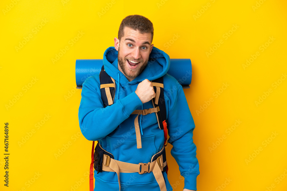 Young caucasian mountaineer man with a big backpack isolated on yellow background celebrating a victory Young caucasian mountaineer man with a big backpack isolated on yellow background celebrating a victory