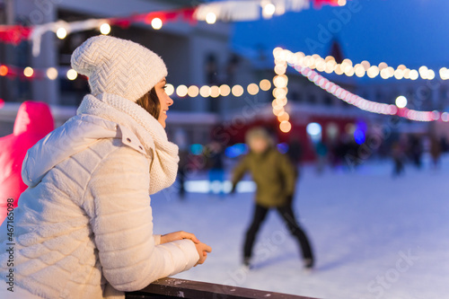 Christmas, winter and leisure concept - happy young woman near ice skating rink outdoors.