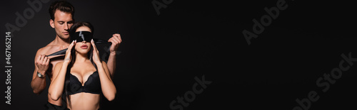 Wallpaper Mural shirtless man covering eyes of sexy woman with silk blindfold isolated on black, banner Torontodigital.ca