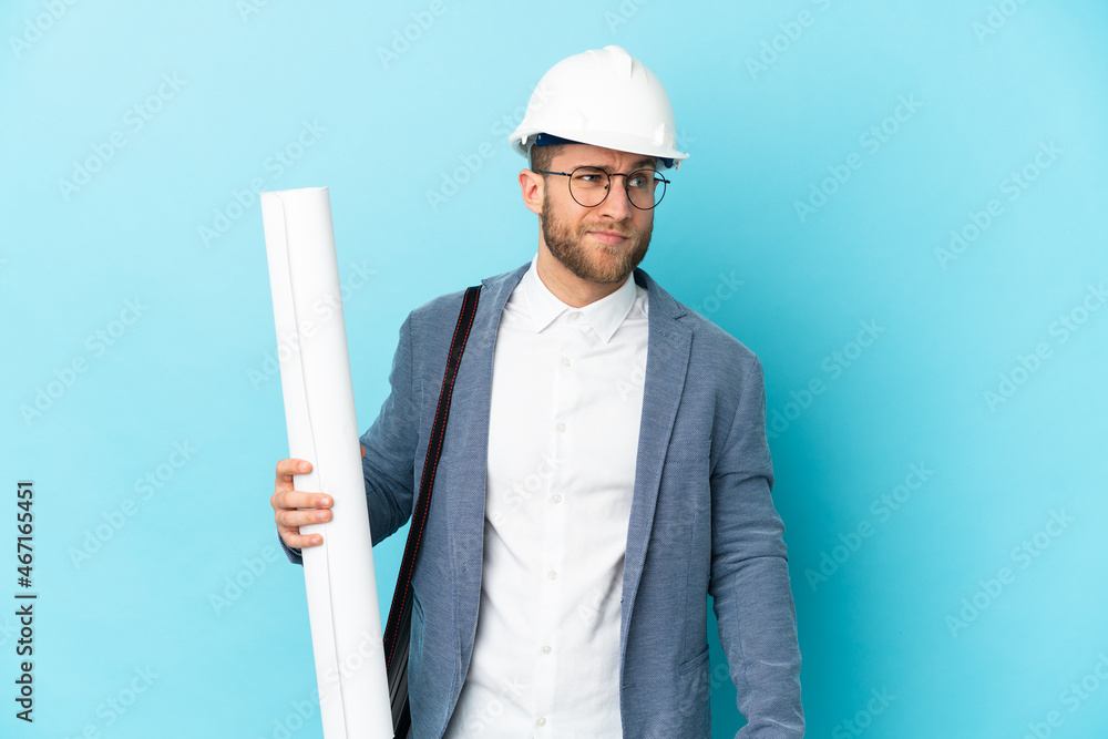 Young architect man with helmet and holding blueprints over isolated background having doubts and thinking Young architect man with helmet and holding blueprints over isolated background having doubts and thinking