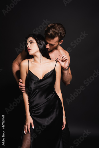 shirtless man touching strap of silk dress on passionate woman on black