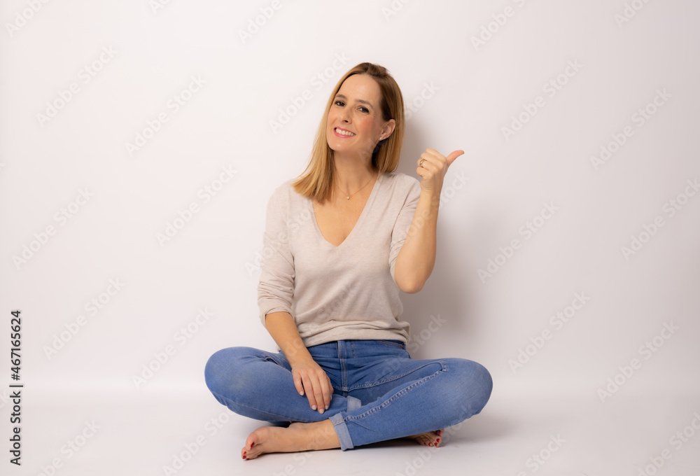 Smiling woman sitting on floor cross-legged with thumb up isolated over white background. Smiling woman sitting on floor cross-legged with thumb up isolated over white background.