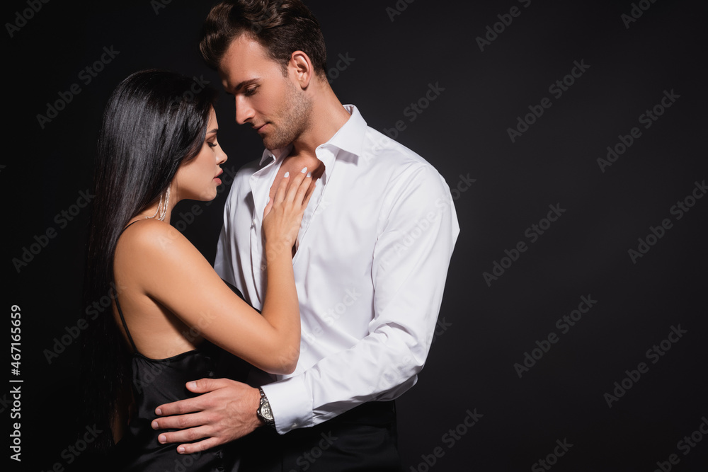 young man in white shirt hugging waist of elegant woman isolated on black young man in white shirt hugging waist of elegant woman isolated on black