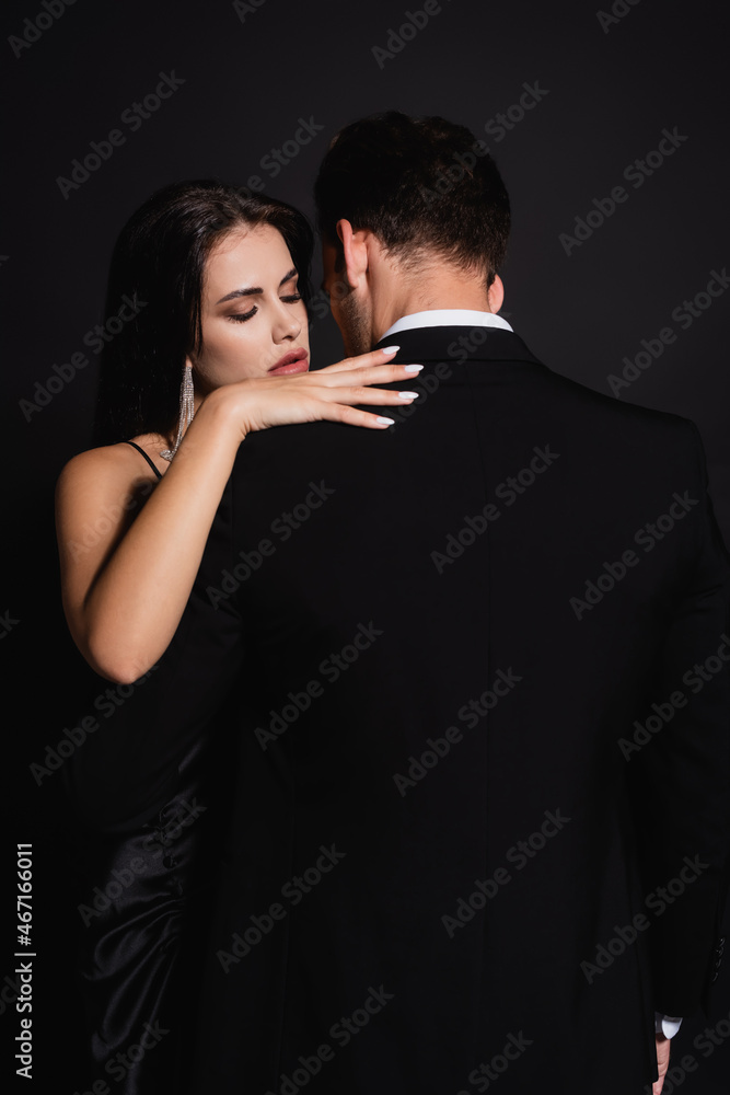 back view of man in suit near elegant woman hugging him isolated on black back view of man in suit near elegant woman hugging him isolated on black