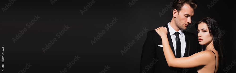 seductive woman touching shoulder of man in suit isolated on black, banner seductive woman touching shoulder of man in suit isolated on black, banner