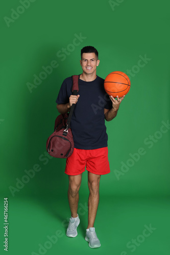 Handsome man with sports bag and basketball ball on green background © New Africa