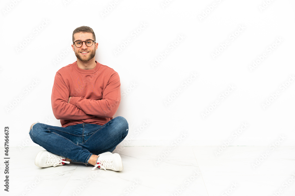 Young handsome man sitting on the floor keeping the arms crossed in frontal position
