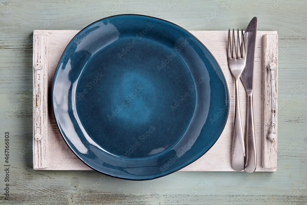 Handmade blue ceramic plate with cutlery on a white wooden tray Handmade blue ceramic plate with cutlery on a white wooden tray