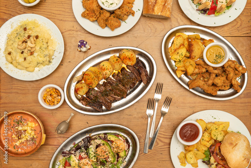 selection of international dishes, gnocchi with cheese and nuts, grilled beef, hamburger with potatoes, breaded chicken strips, prawn cocktail, forks