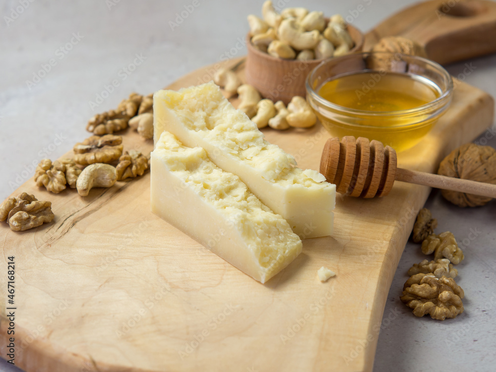 slices of hard cheese on a wooden board with nuts and honey the best combination