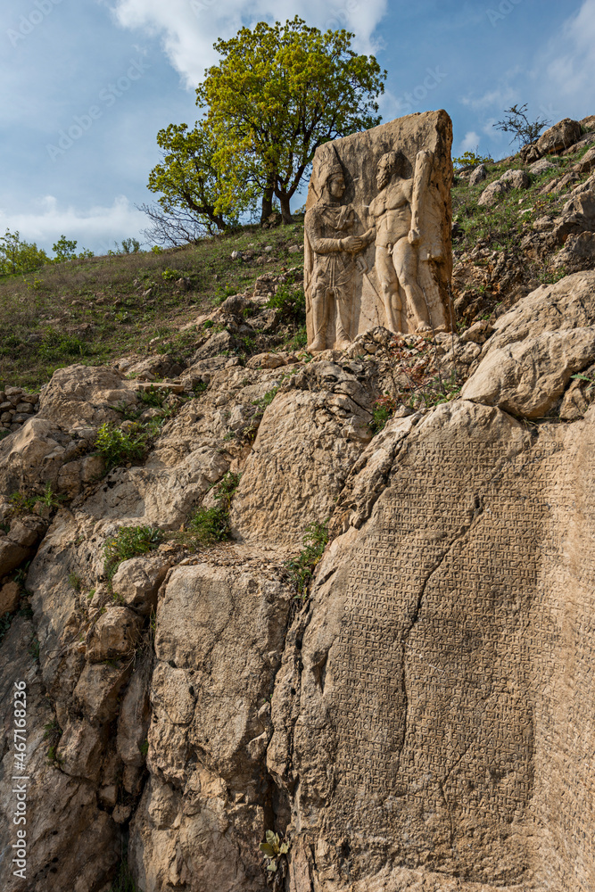 stone sculptures of Greek deities with stone wall full of sculpted scriptures on the foothills of the Mountain of the Gods