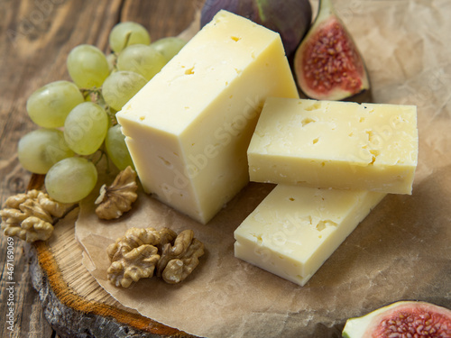 farm quality cheese lie on a wooden board surrounded by figs. grapes and nuts. close-up on an old wooden table