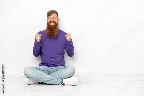 Young caucasian reddish man sitting on the floor isolated on white background celebrating a victory in winner position
