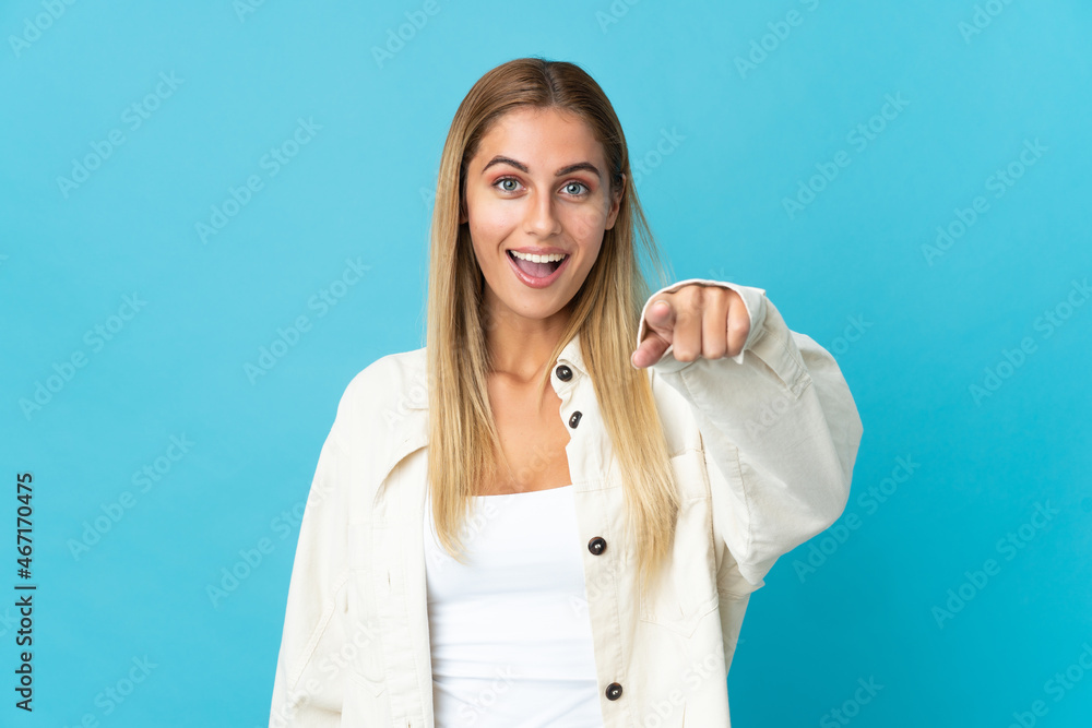 Young blonde woman isolated on blue background surprised and pointing front Young blonde woman isolated on blue background surprised and pointing front