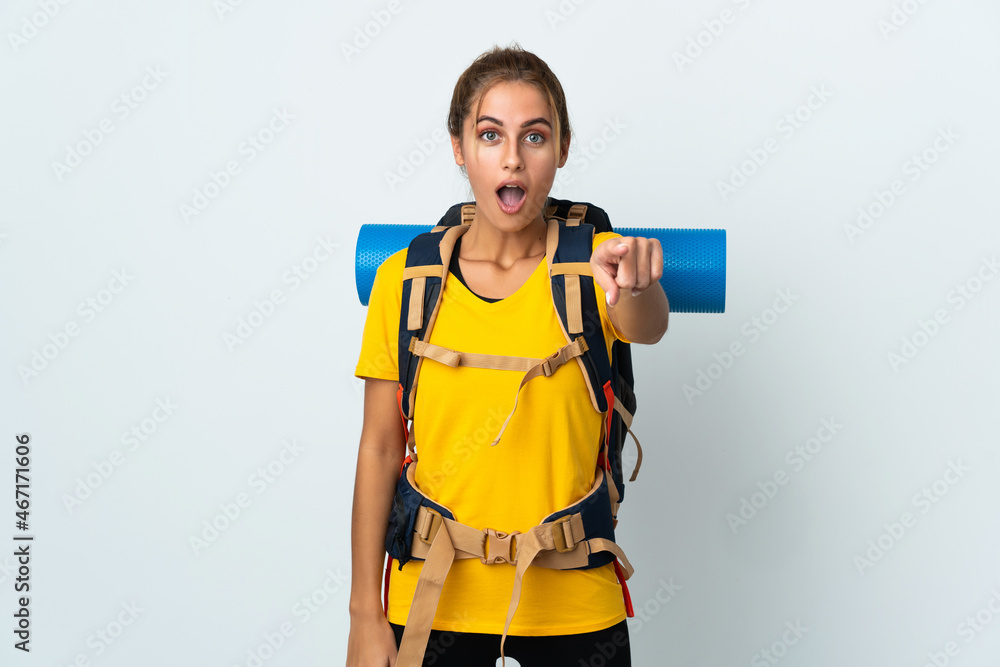 Young mountaineer woman with a big backpack isolated on white background surprised and pointing front