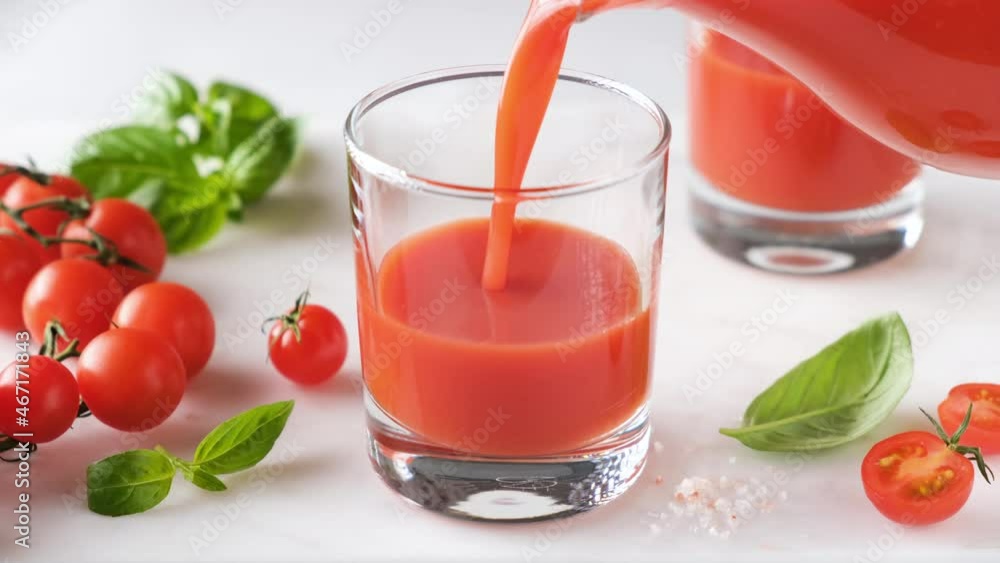 Pouring tomato juice in a glass on a marble background. Healthy vegan nutritious drink Pouring tomato juice in a glass on a marble background. Healthy vegan nutritious drink