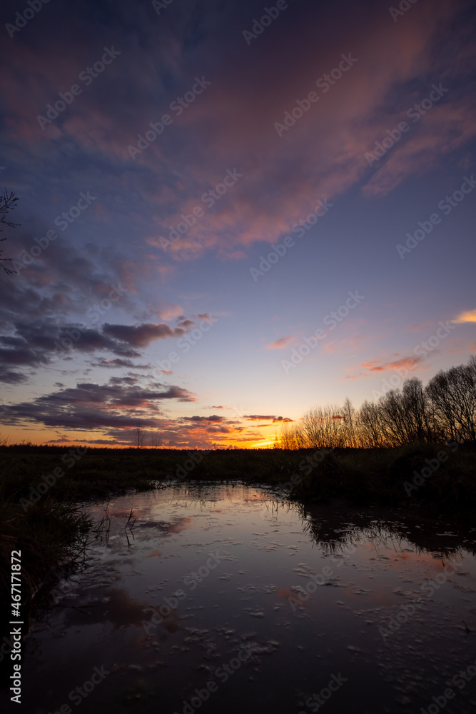 Obraz premium a beautiful blue lake with some tree silhouettes in the foreground under a dramatic sunset sky. High quality photo