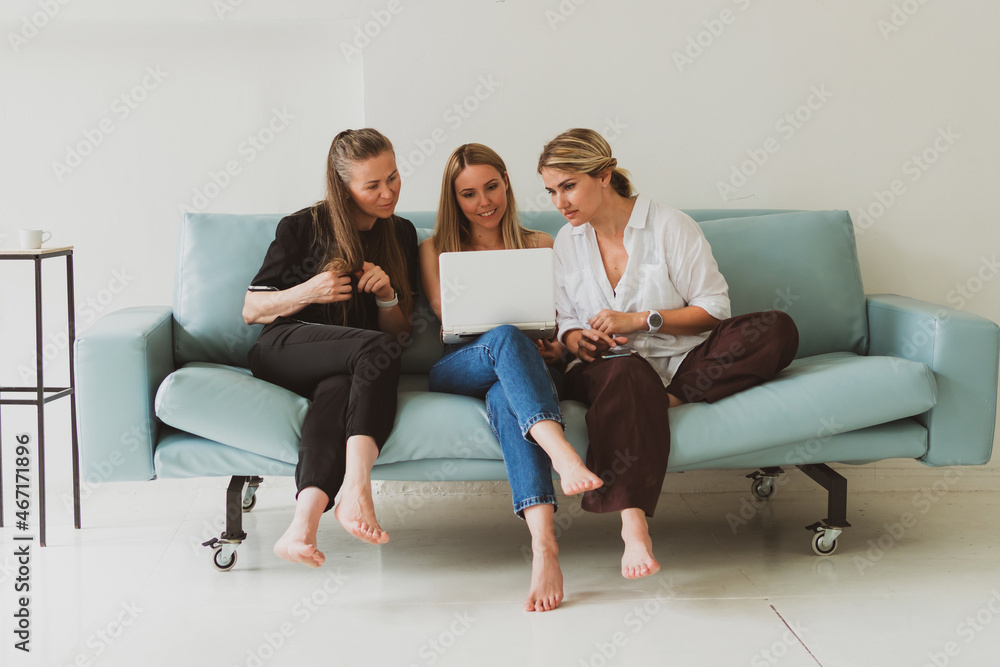 three young attractive women at home on the couch talking while looking at the laptop