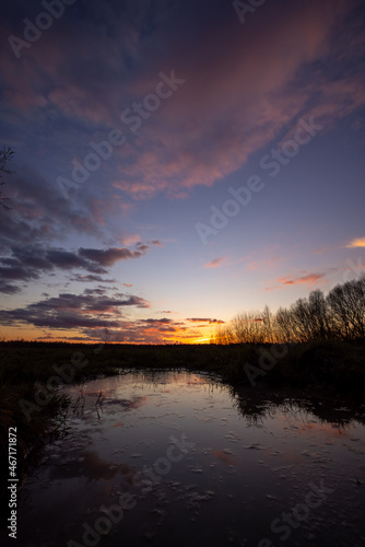 a beautiful blue lake with some tree silhouettes in the foreground under a dramatic sunset sky. High quality photo