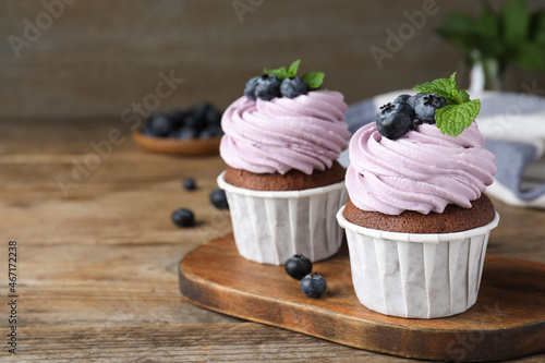 Sweet cupcakes with fresh blueberries on wooden table. Space for text