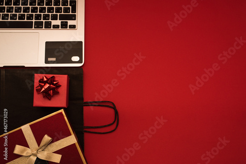 Creative look, red gift box, laptop, credit card and black package on red background, place for text. Black friday, discounts, online shopping day of sale, christmas shopping on a red background top