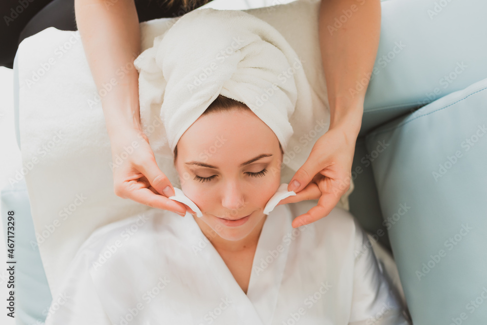 beautician makes facial and massage to a young woman with a towel on her head