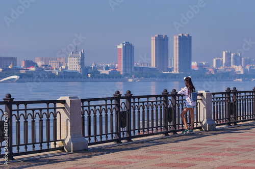 Fotografia A young girl with a backpack admires the view of the city of Heihe, China from the embankment of the city of Blagoveshchensk, Russia