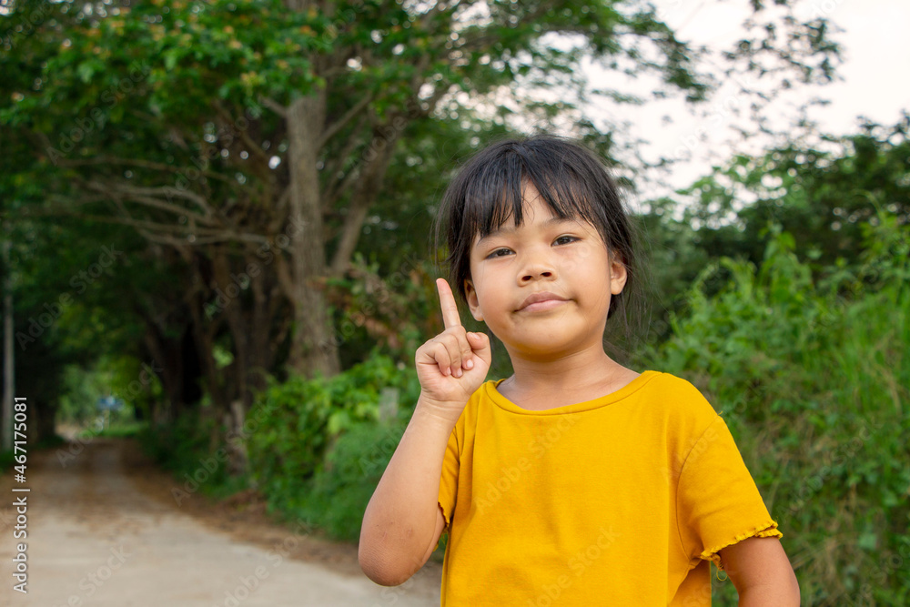 portrait of a cute little Asian girl standing smiling and index finger up in the natural background. Happy, healthy, and clever child concept
