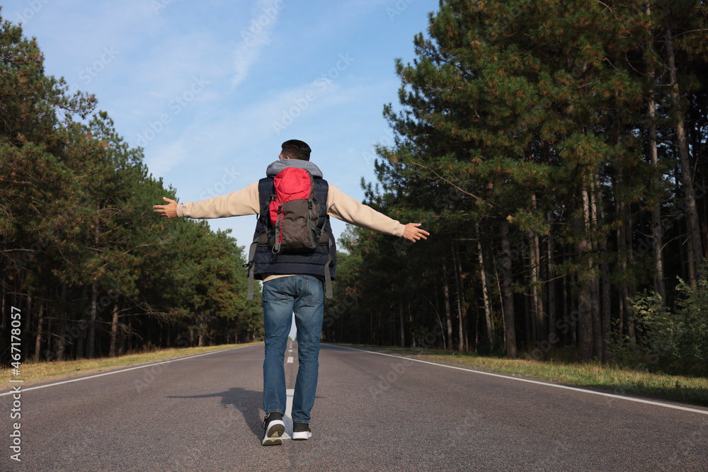 Fototapeta premium Man with backpack going along road near forest, back view