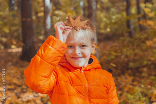 Portrait of happy child boy in orange jacket in autumn park. Fall season and children concept