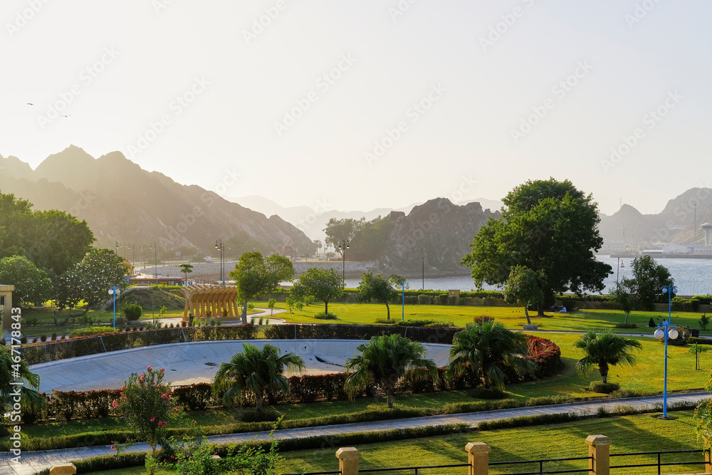 Park with a green lawn and big trees, mountain and sky background, Oman Muscat tourism, no people.
