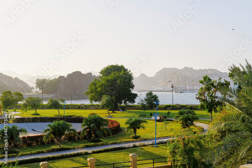 Qurum park with a green lawn and big trees, mountain and sky background, Oman tourism, no people.