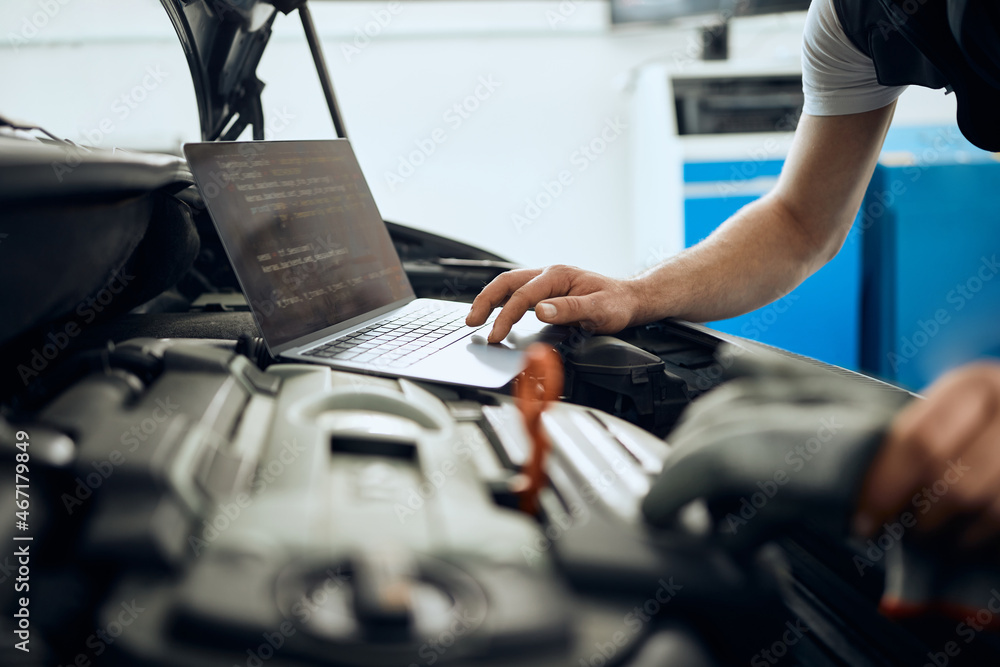 Close-up of auto mechanic uses laptop while examining car engine at service workshop. - obrazy, fototapety, plakaty 