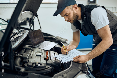 Auto mechanic writes data during engine maintenance at car service workshop.