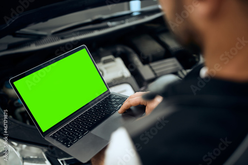 Close- up of car mechanic uses laptop while examining engine performance at workshop photo