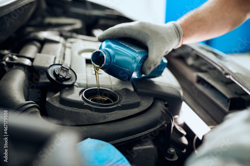 Close- up of mechanic pours motor oil while doing car engine maintenance at auto repair shop.