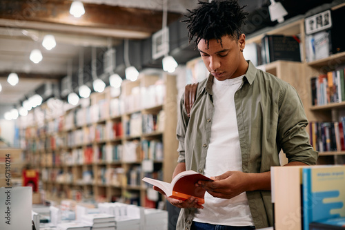 Young African American student reads book while standing at bookstore. photo